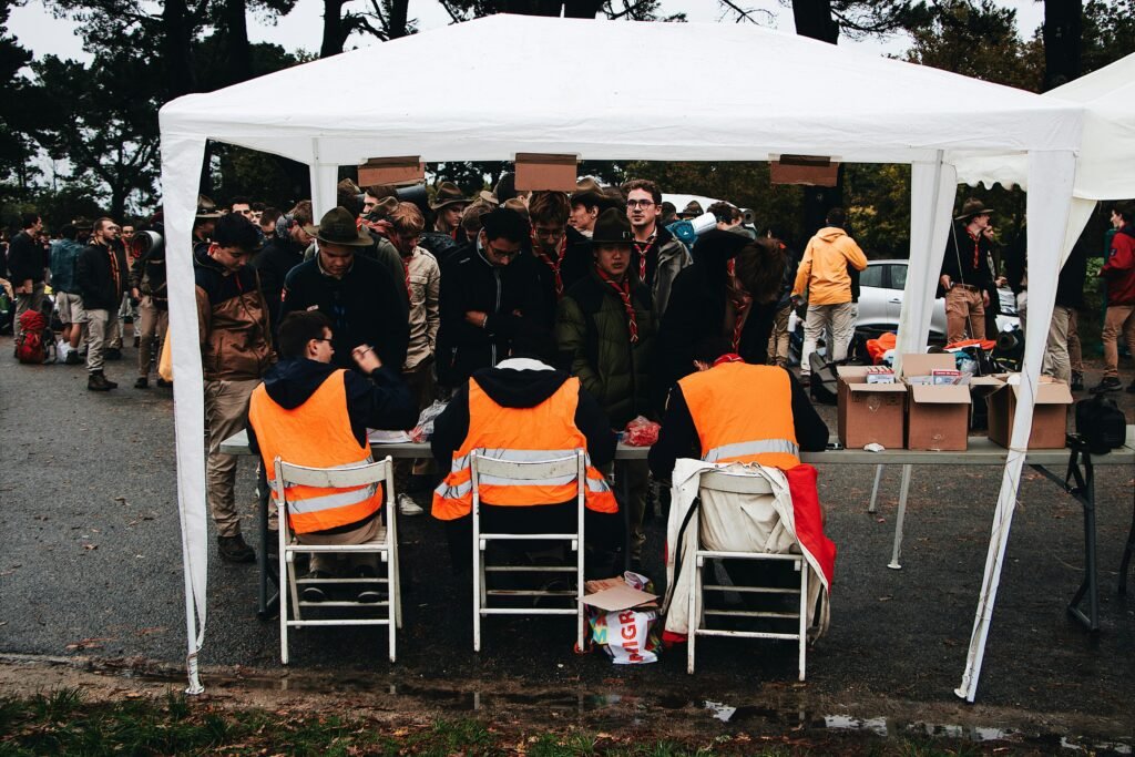 pexels photo 3195786 3195786 Crowded outdoor check-in tent at an event with attendees in fluorescent vests and scout uniforms.